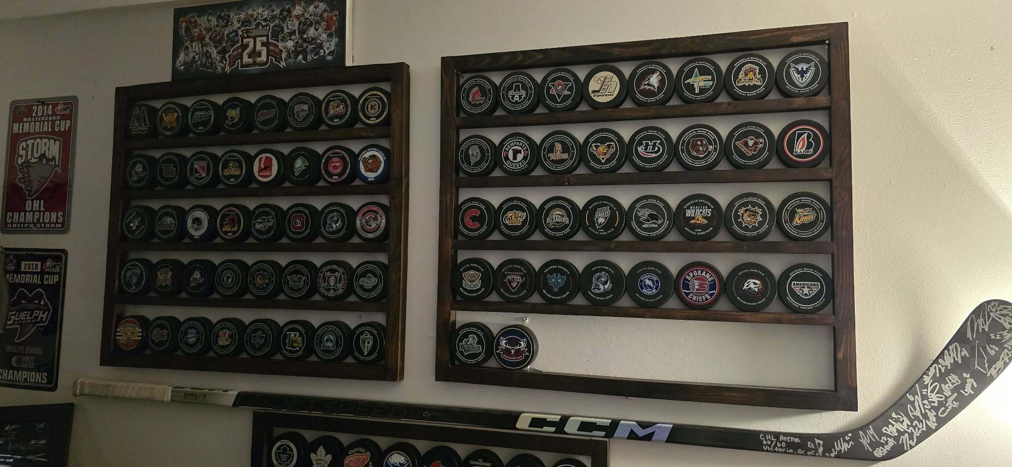 A photo of Steve McLean’s puck shelves, with each puck representing a CHL building and team he’s seen, arranged in chronological order, alongside the stick he received from the Royals.