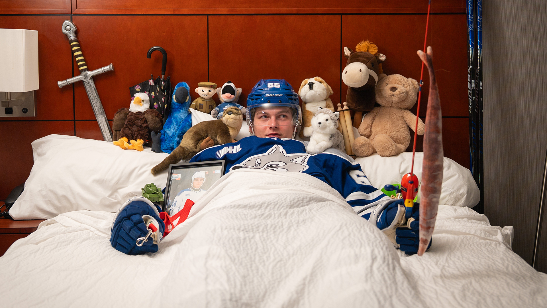 JC Lemieux in full hockey gear, in a bed surrounded by various plush toys (and a framed photo of Daniel Berehowsky).